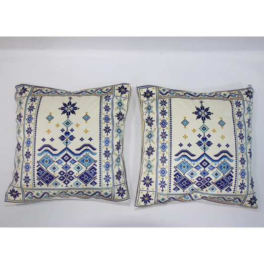 Two square decorative throw pillows with cream backgrounds and intricate blue, navy, and gold embroidered geometric patterns, displayed side-by-side against a plain white background.