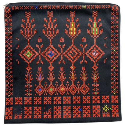 A square black zippered pouch featuring a vibrant, traditional geometric cross-stitch pattern in red, orange, yellow, green, and blue thread, photographed flat against a white background.