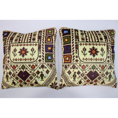 Two square decorative throw pillows with traditional geometric and floral patterns in cream, brown, and multicolor accents, displayed side-by-side against a plain light gray background.