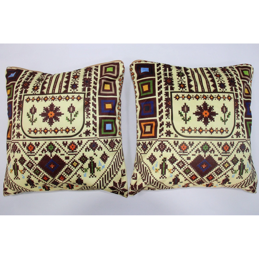 Two square decorative throw pillows with traditional geometric and floral patterns in cream, brown, and multicolor accents, displayed side-by-side against a plain light gray background.