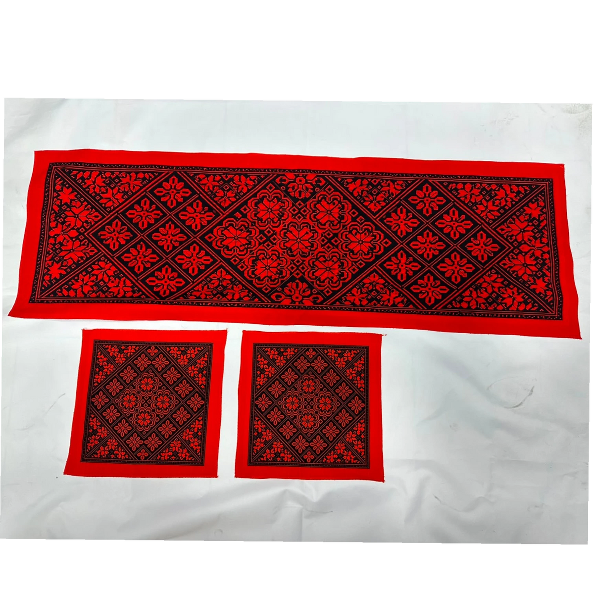 A set of three red and black embroidered textile pieces, including one long rectangular runner and two smaller square pieces, laid flat on a white background.